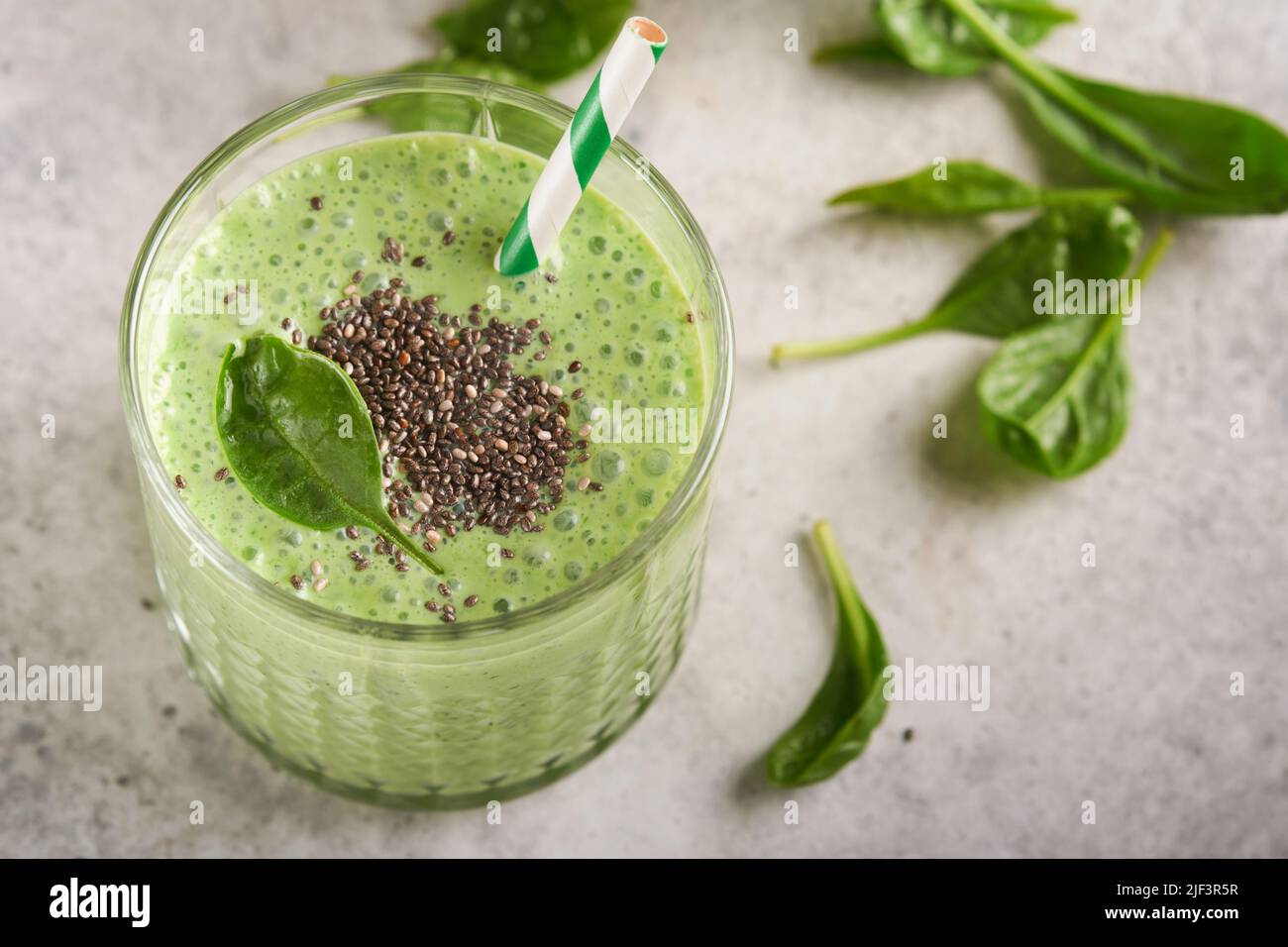 Spinach smoothie healthy green. Vegan smoothie or milkshake from spinach, banana and chia seeds on gray concrete table background. Clean eating, alkal Stock Photo