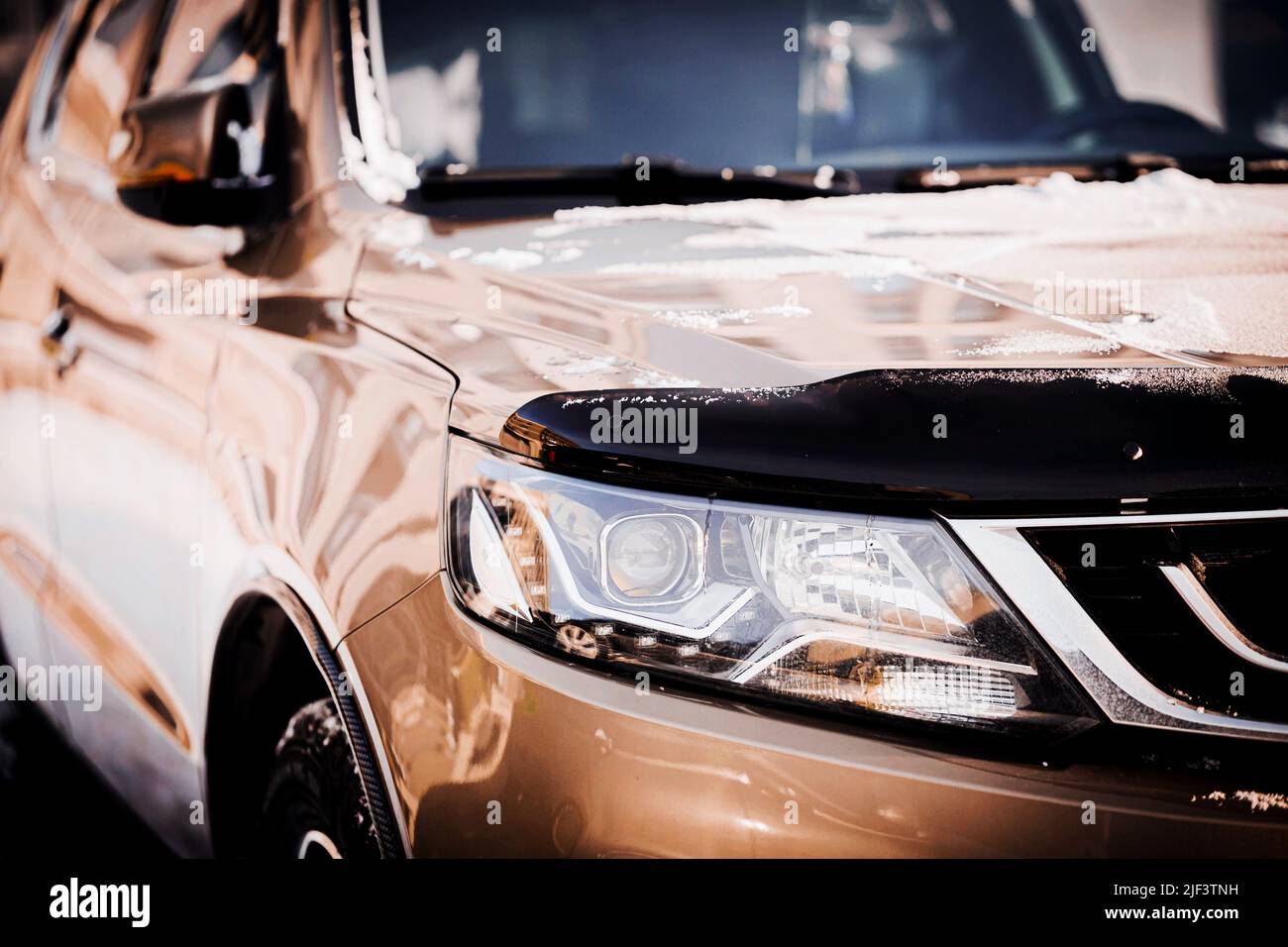The front part of a new polished beautiful silver-colored car with snow on the bumper on a sunny day. Transport in winter. Stock Photo