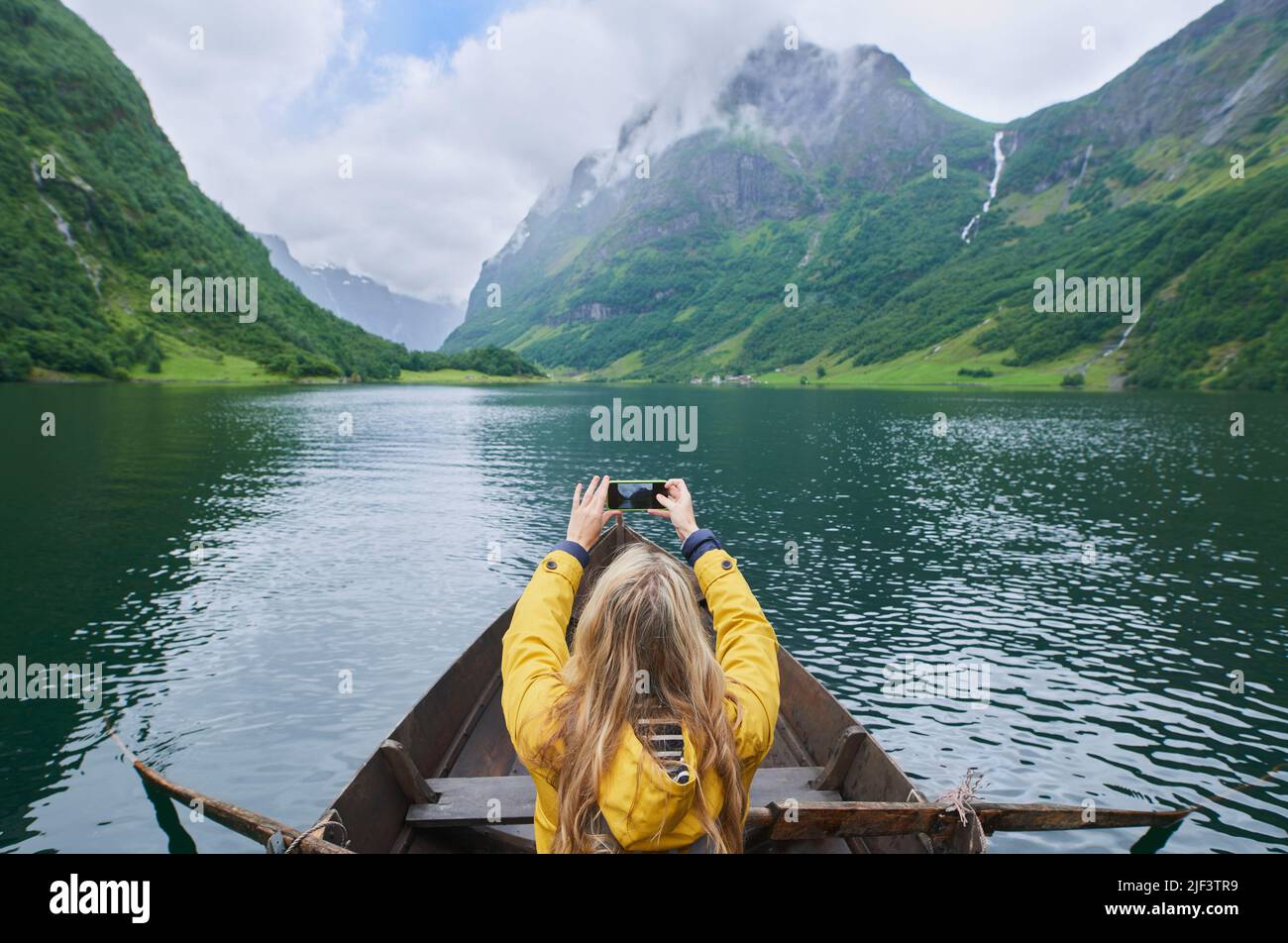 Adventure woman in row boat taking photo on smart phone of beautiful fjord lake for social media Stock Photo