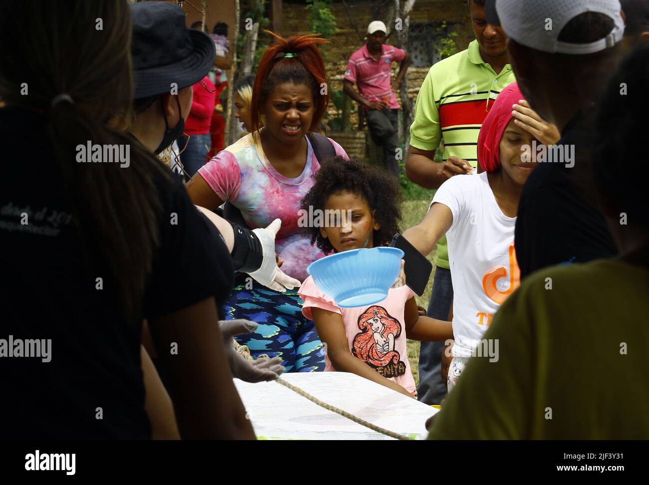 Valencia, Carabobo, Venezuela. 25th June, 2022. Junio 25, 2022. Una niÃ±a entrega un envase para ser llenado de sopa por miembros de la asociacion sin fines de lucro y con actividades netamente humanitarias ''Dar mas que recibir'' quienes celebraron su octavo aniversario con un operativo donde, donaron ropa, juguetes, las tradicionales arepas y el sancocho comunitario. También frcieron servicio de peluqueria, servicio medico de pediatria, odontologia, ginecologia, nutriciÃ³n, hematologia, y actividades recreativas para los niÃ±os, quienes al final cantaron cumpleaÃ±os y comieron torta. jun Stock Photo