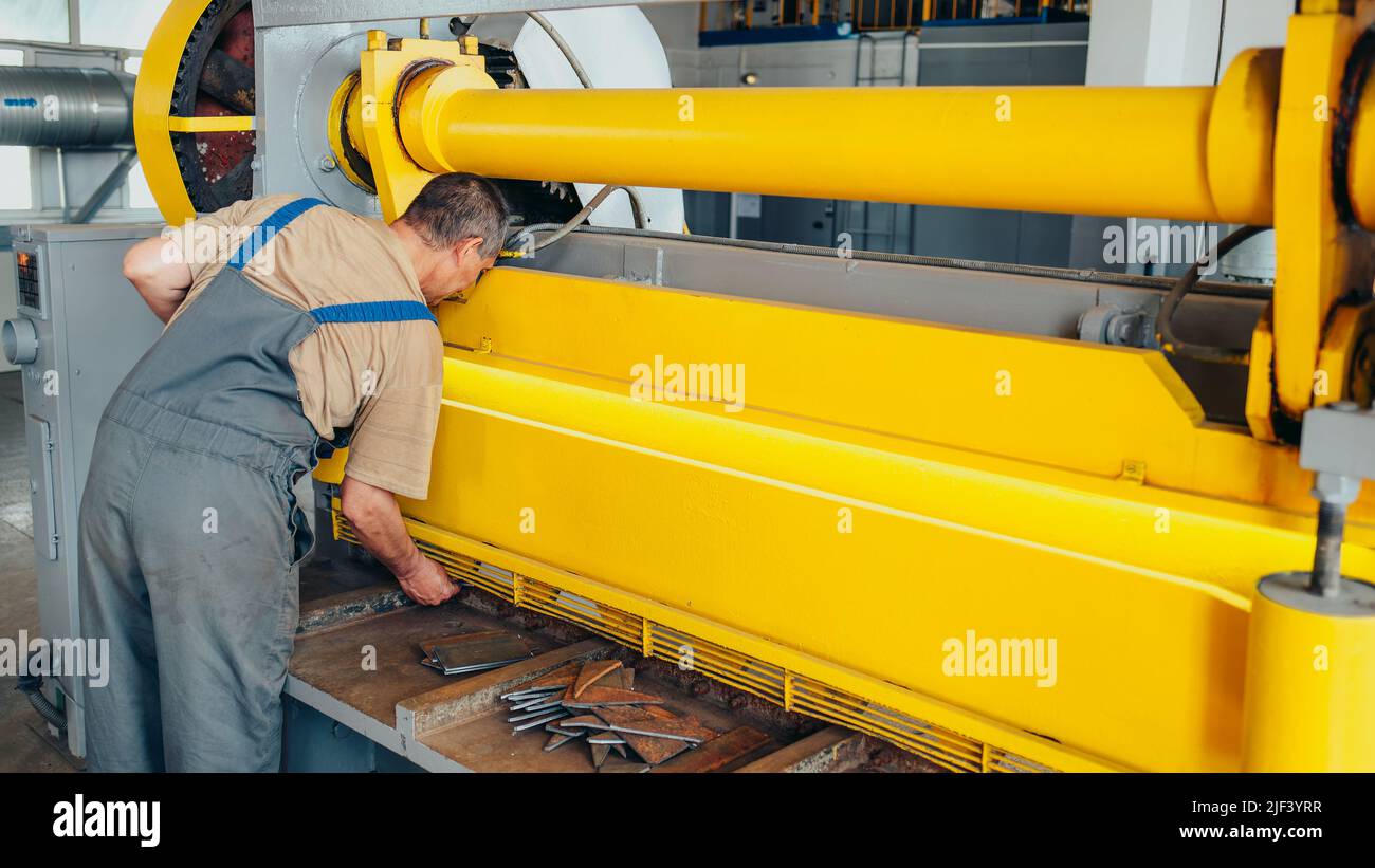 Worker cuts metal sheets on mechanical guillotine machine in production hall. Industrial equipment for metal cutting. Real scene. Real workflow. Man at work. Stock Photo