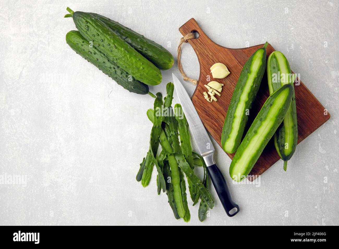 Fresh cucumbers with skin and knife on a brown wooden cutting board on a light gray concrete table Stock Photo