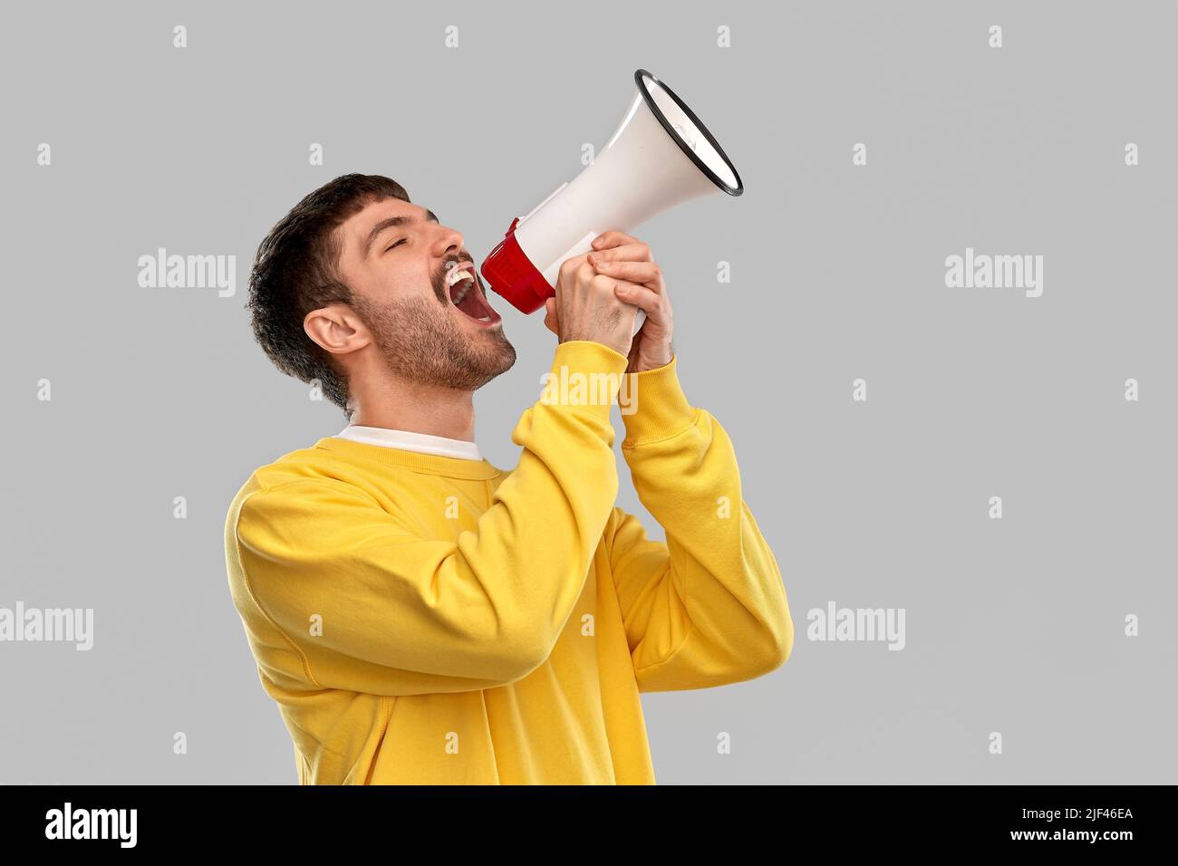 man in yellow sweatshirt shouting to megaphone Stock Photo