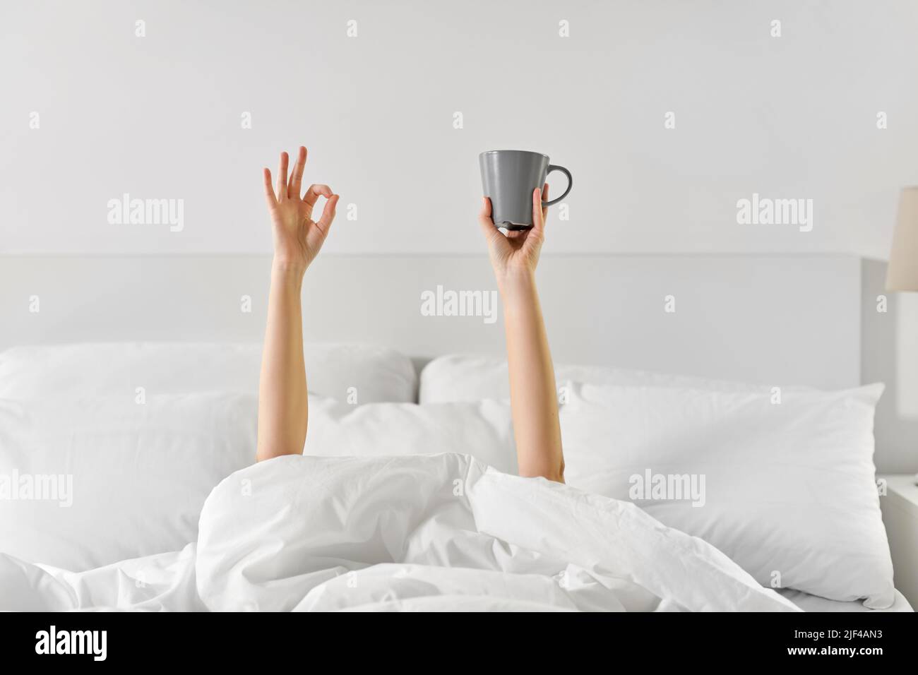 woman with cup of coffee lying in bed showing ok Stock Photo Alamy