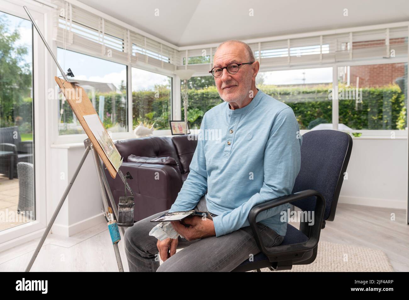 Environmental portrait of a senior  man painting with watercolours in his home studio Stock Photo