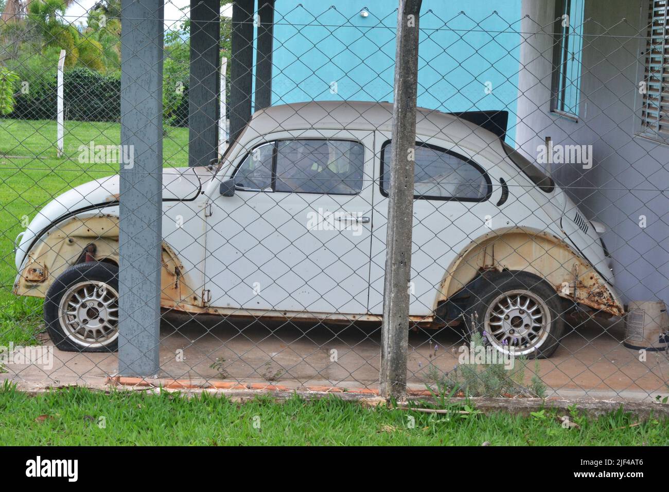 Beetle, old semi-destroyed vehicle in white color with light alloy wheels in masonry garage in panoramic style photo in farmland in Brazil, South Amer Stock Photo