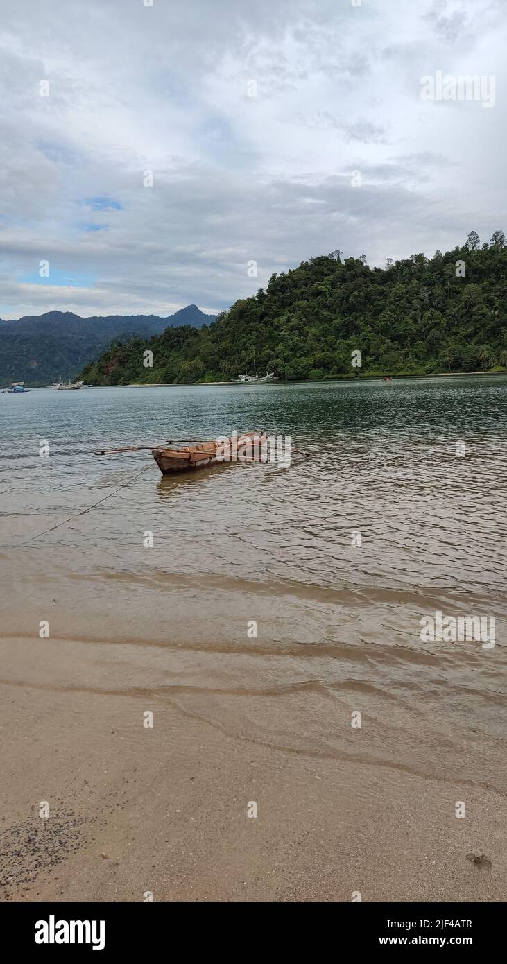 Vertical shot of a wooden boat in bay moored to the shore the backdrop ...