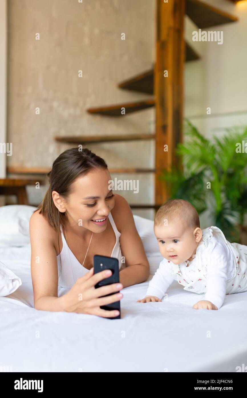 A young mother with her newborn daughter during an online video chat with her father. A woman shows their daughter to dad, smiles and communicates wit Stock Photo