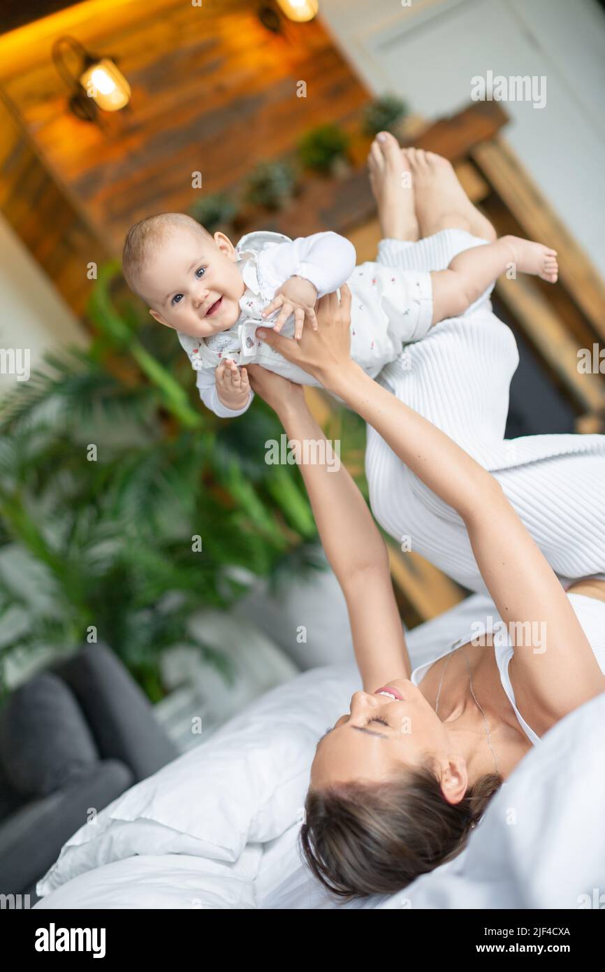 Young mother and her baby girl having playing and having fun in bed. Vertical photo. Stock Photo