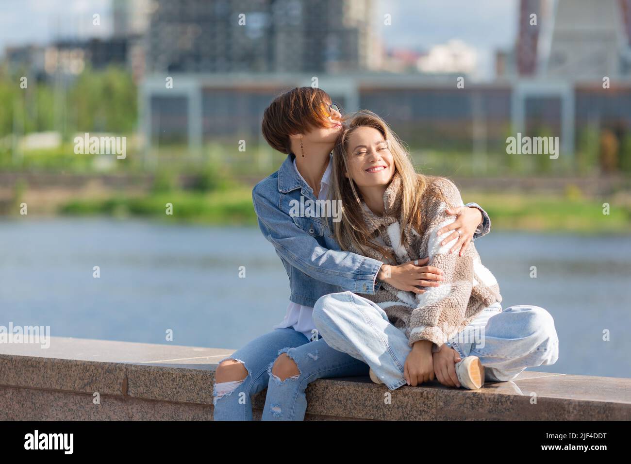 Love and relationships concept. Lesbian couple sit on the embankment and enjoy each other. Beautiful romantic moment between two female lovers. Stock Photo