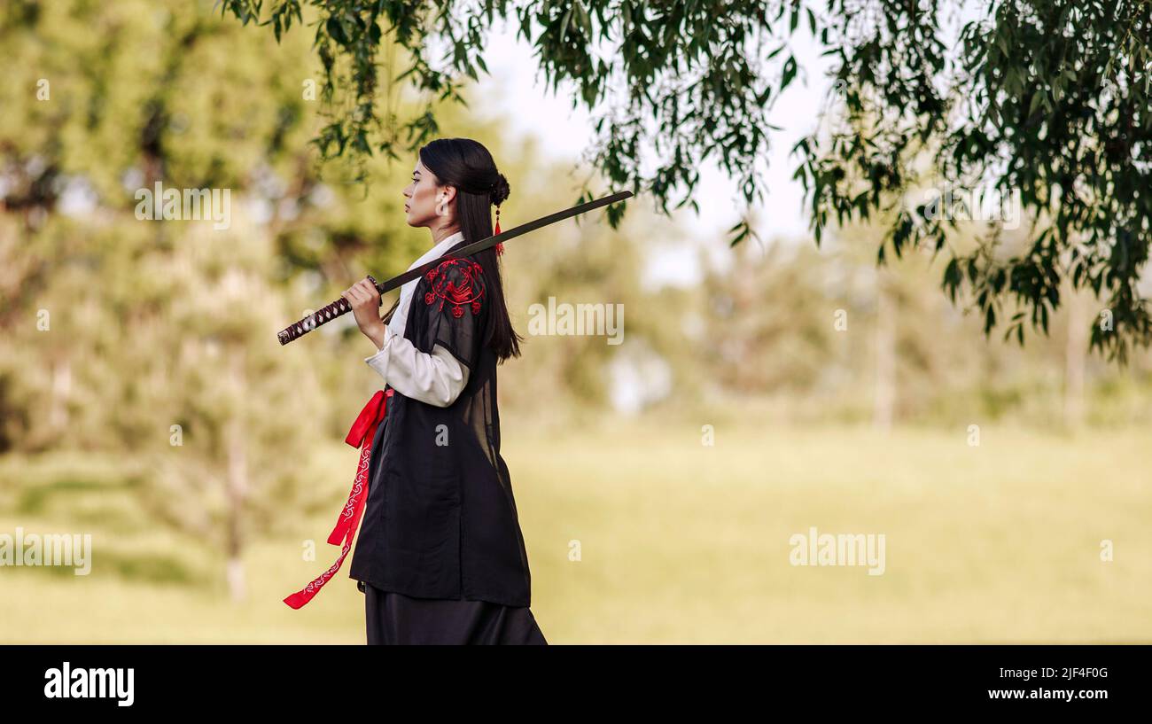 Young asian woman in traditional kimono trains in a fighting stance close-up portrait with katana sword samurai warrior girl in green summer garden Stock Photo