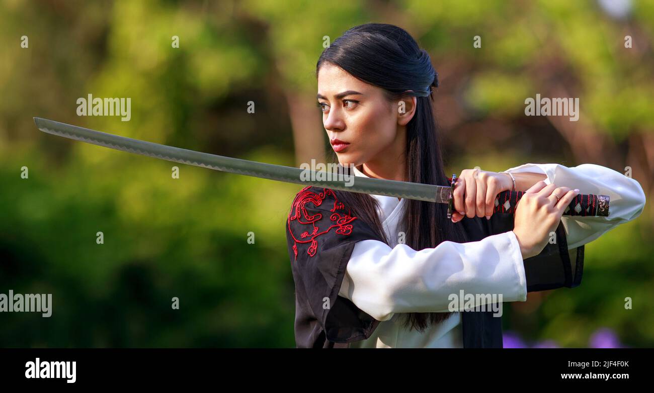 Young asian woman in traditional kimono trains in a fighting stance close-up portrait with katana sword samurai warrior girl in green summer garden Stock Photo