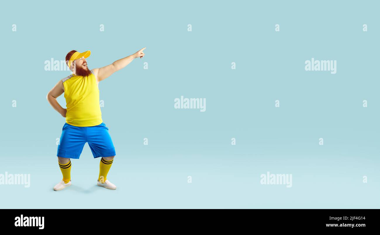 Funny fat man dressed for fitness workout dancing and pointing to copy space background Stock Photo