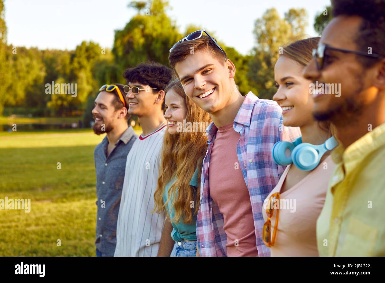Portrait of joyful young man standing with his friends hanging out in public park. Stock Photo