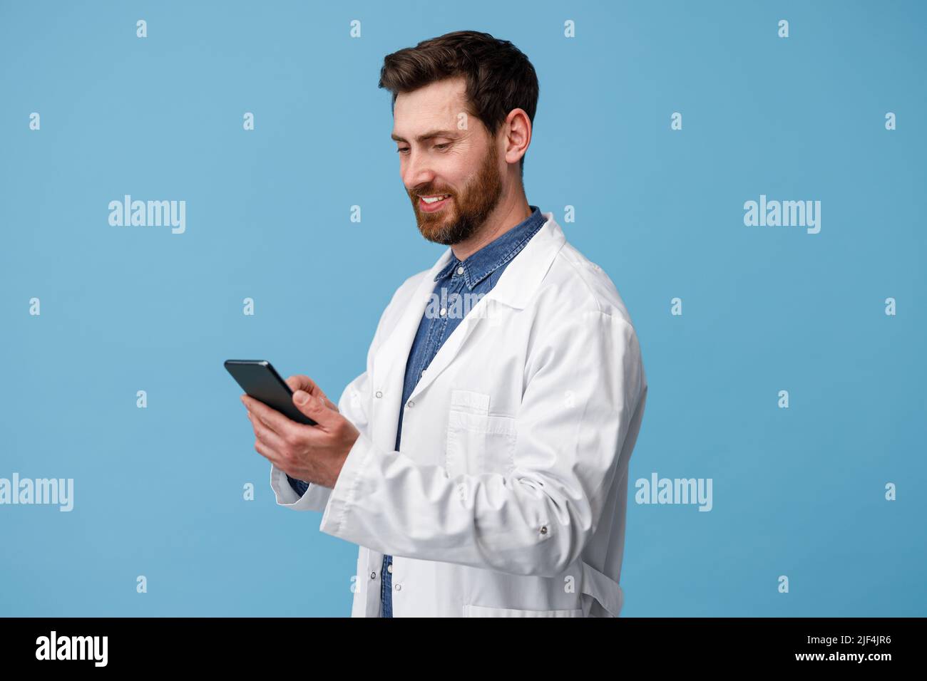 Smiling medical specialist using mobile phone over blue studio background Stock Photo