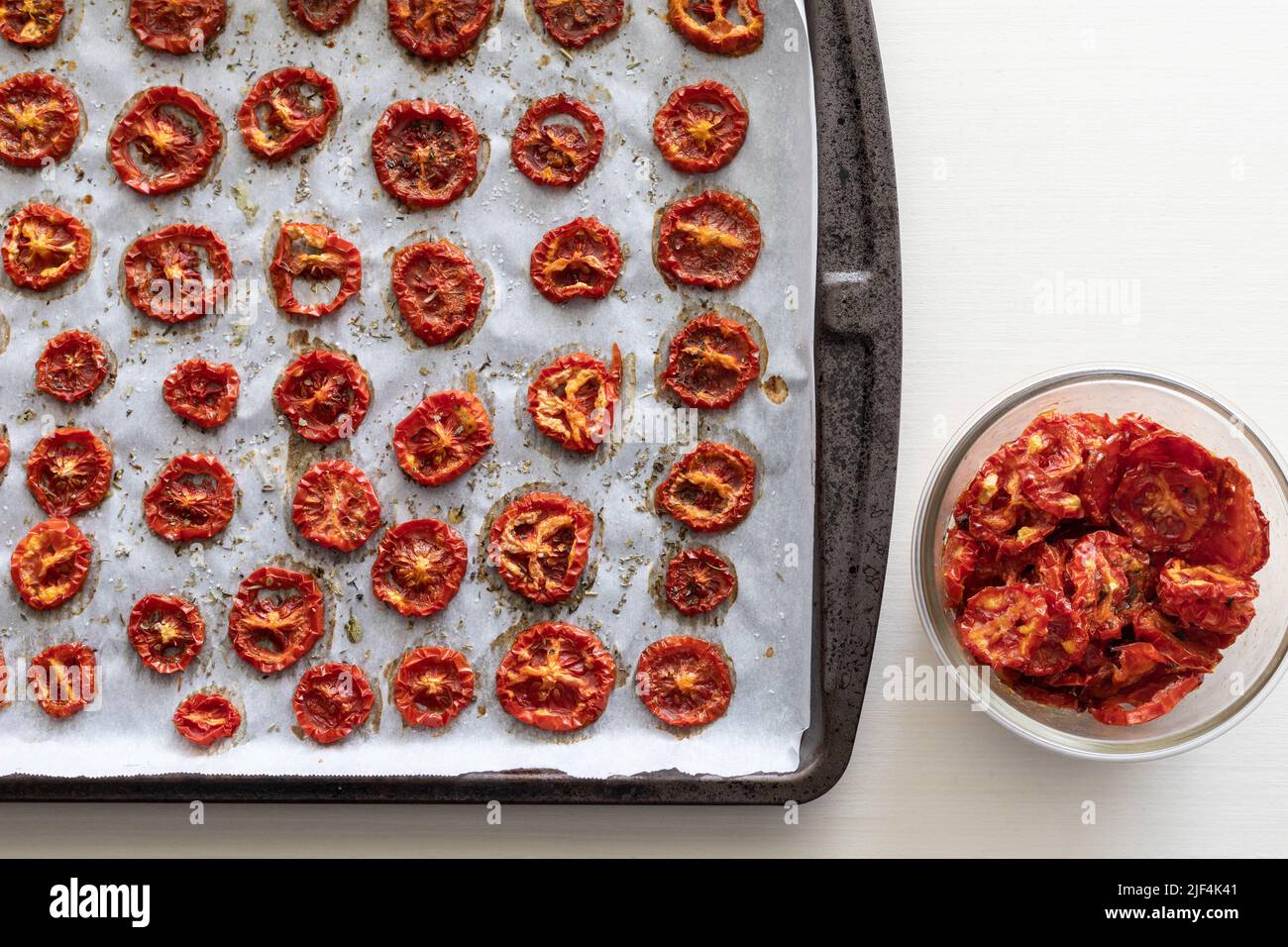 Freshly Dried Tomatoes with Herbs on Cookie Sheet and in Glass Bowl Stock Photo