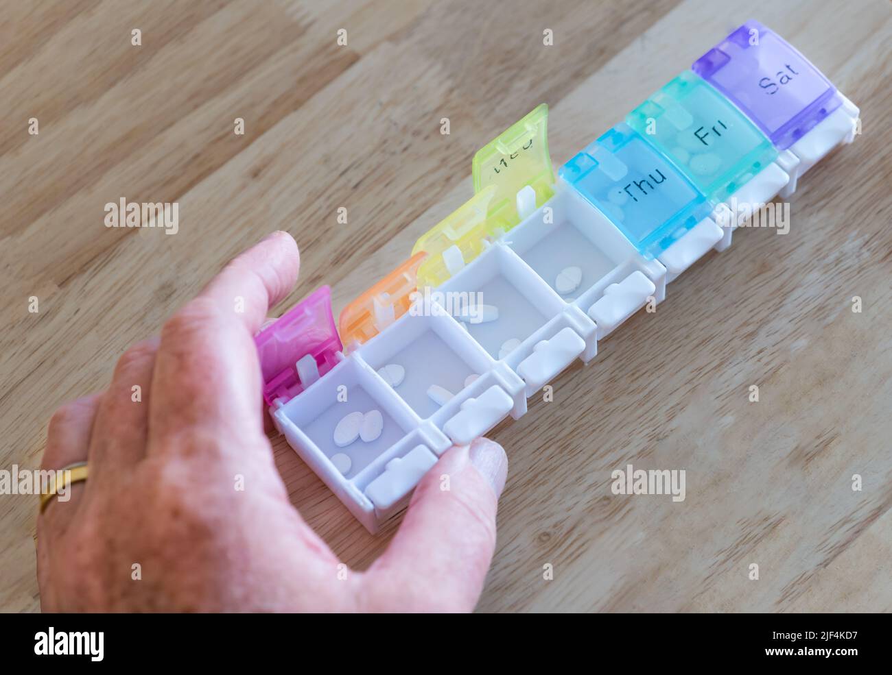 A man organising weekly medication tablets or pills in a pill organiser with days of the week marked, United Kingdom Stock Photo