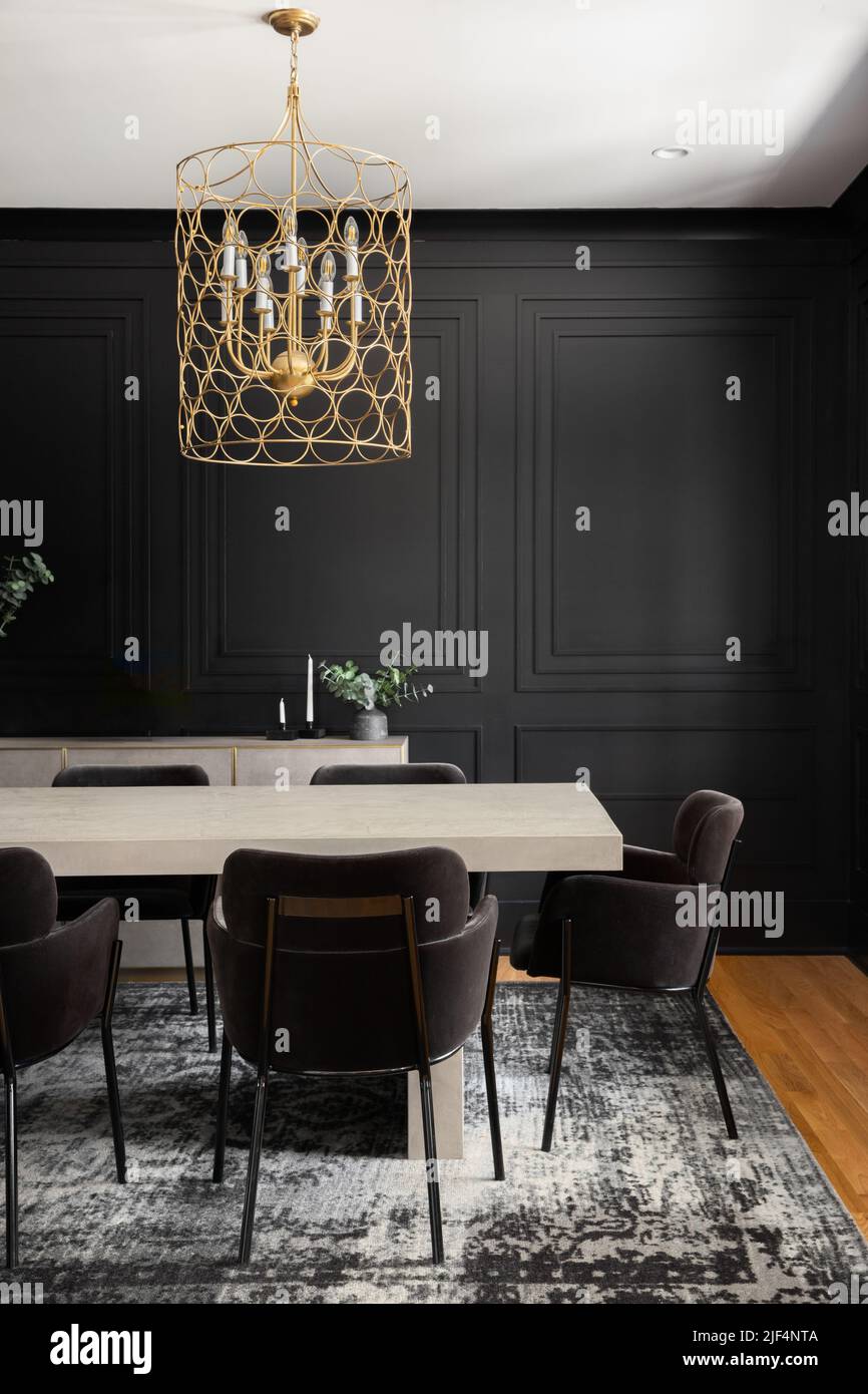 A cozy dining room with a gold chandelier above a wooden table and black wainscoting walls. Stock Photo
