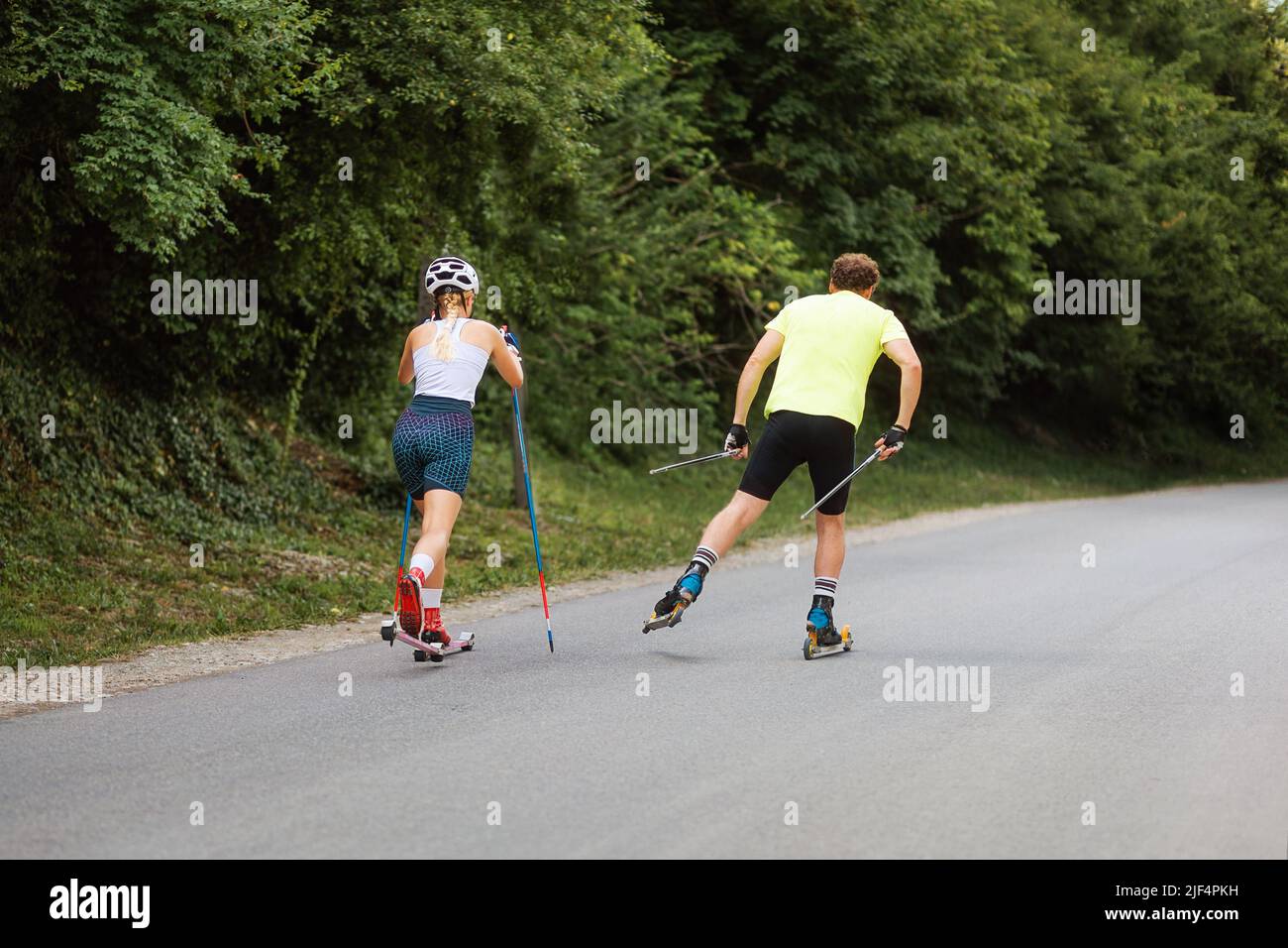 Athletic woman and man together training on the roller ski. Back view. Copy space. Concept of competition, biathlon, and summer workout. Stock Photo