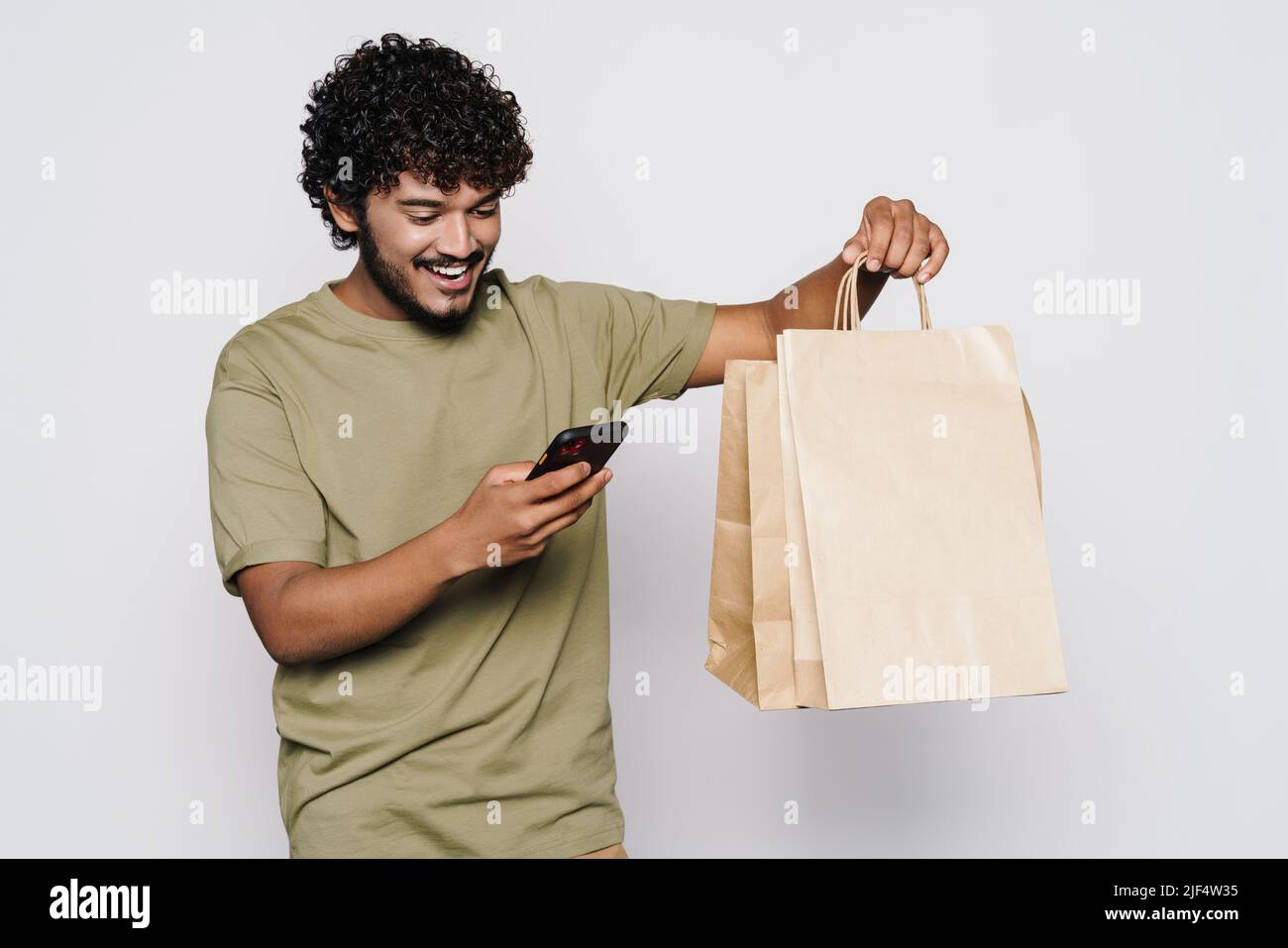 Young middle eastern man with shopping bags using cellphone isolated over white wall Stock Photo