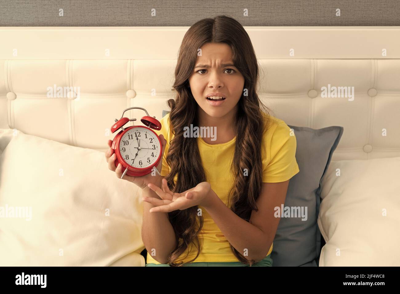 Unhappy girl complain about early hour showing alarm clock in bed, morning time Stock Photo