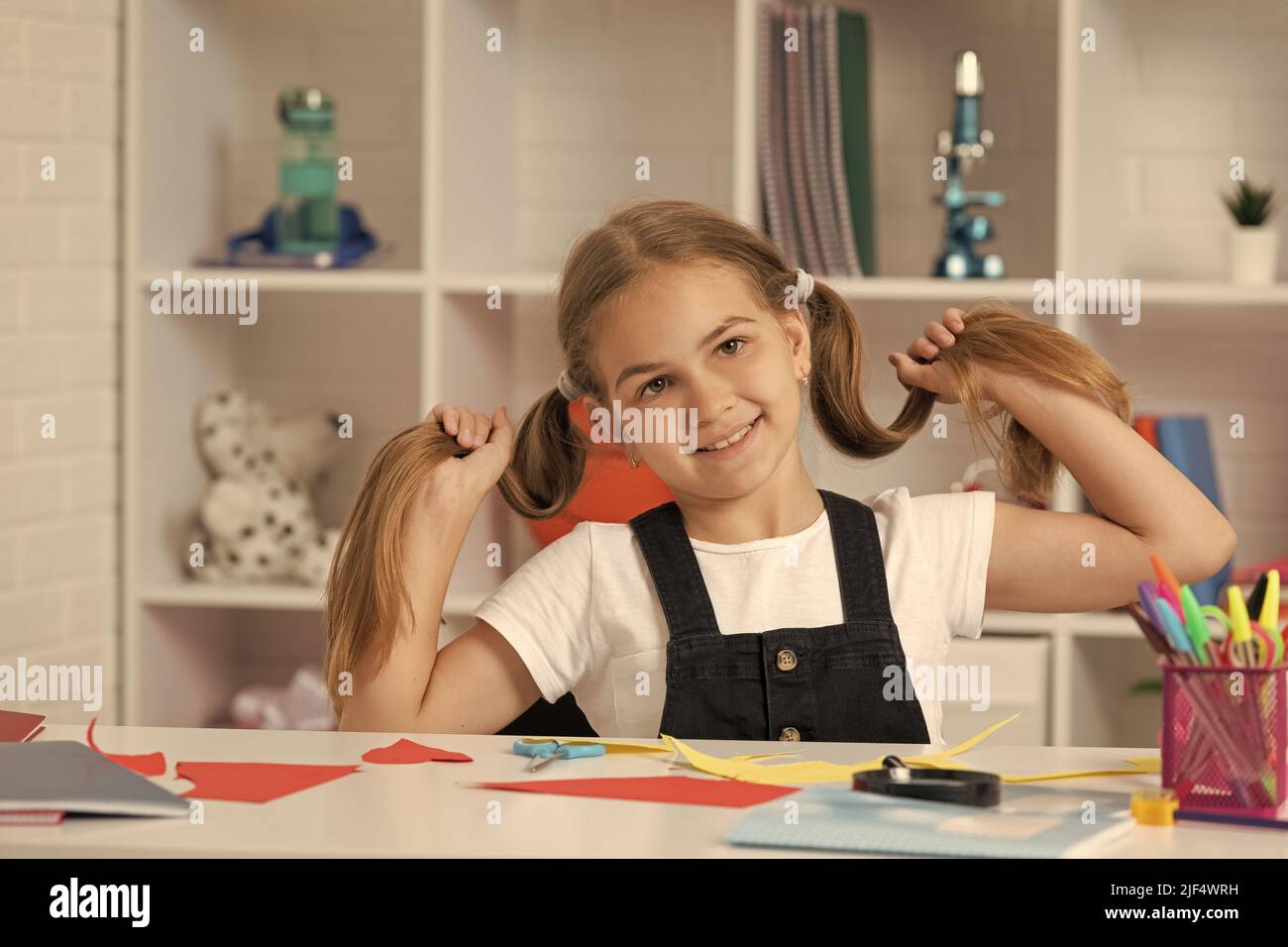 cheerful child having fun with long hair pony tail at school lesson ...