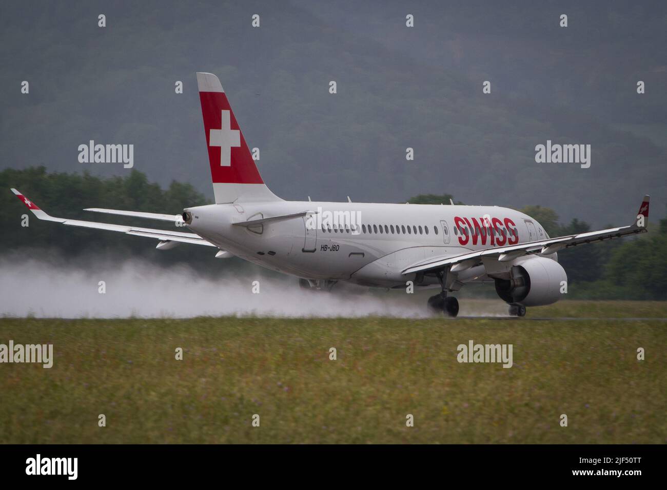 Swiss Airbus A220 departing Graz for a flight to Zurich from a wet runway on a rainy day Stock Photo