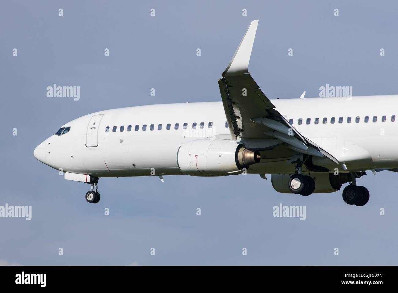 Full white neutralized airliner Boeing 737-800 landing at an airport in front of clear blue sky Stock Photo