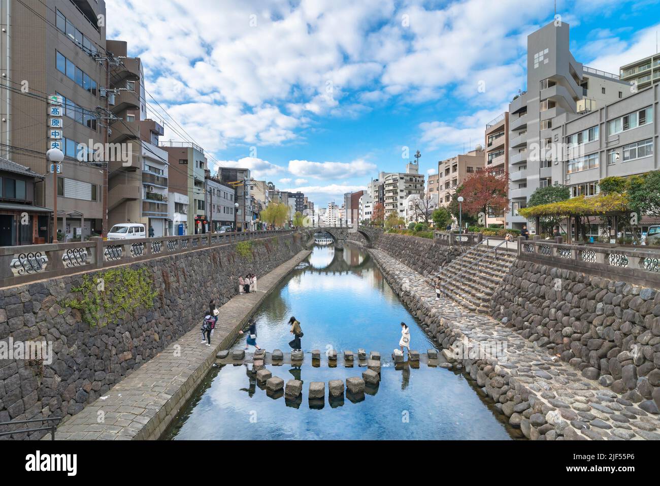 nagasaki, kyushu - december 12 2021: Group of young tourists girls walking on a stone path crossing the Nakashima river in front of Meganebashi or Spe Stock Photo