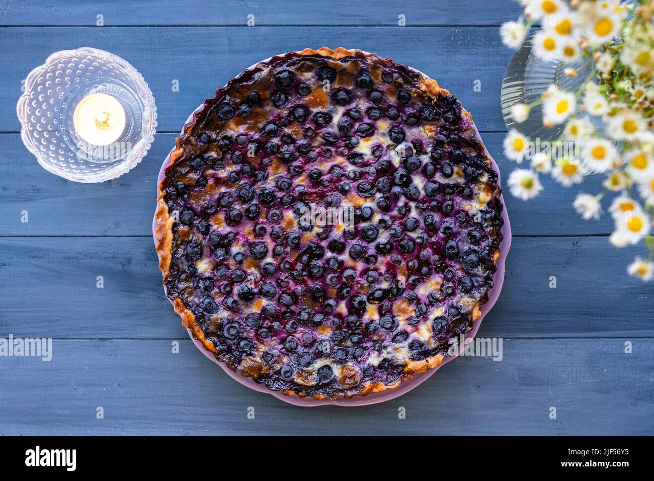 Mustikkapiirakka, a Finnish Blueberry Pie. Flat lay, top view shot on blue wooden table with white flowers. Stock Photo