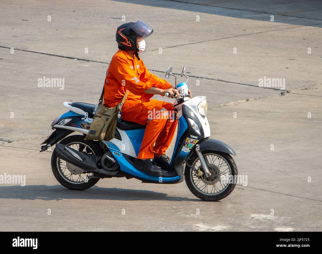 SAMUT PRAKAN,  THAILAND, APR 07 2022, A man dressed in orange overall rides a motorcycle on the city road Stock Photo