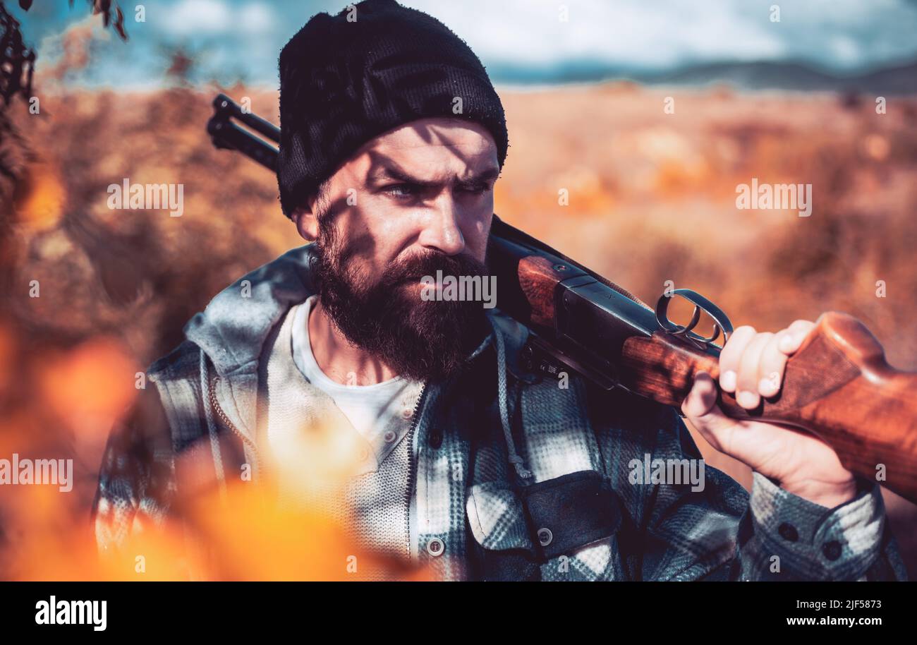 Poacher in the Forest. Bearded hunter man holding gun and walking in forest. Hunting Licenses. Hunter with shotgun gun on hunt. Stock Photo