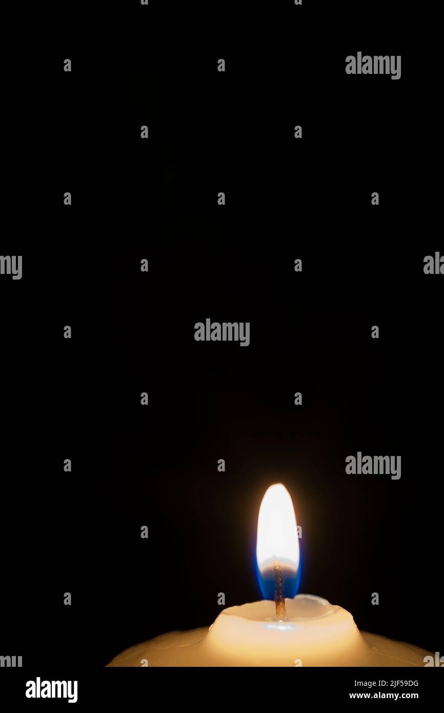 Close-up of white wax candle with blue flame against black background ...