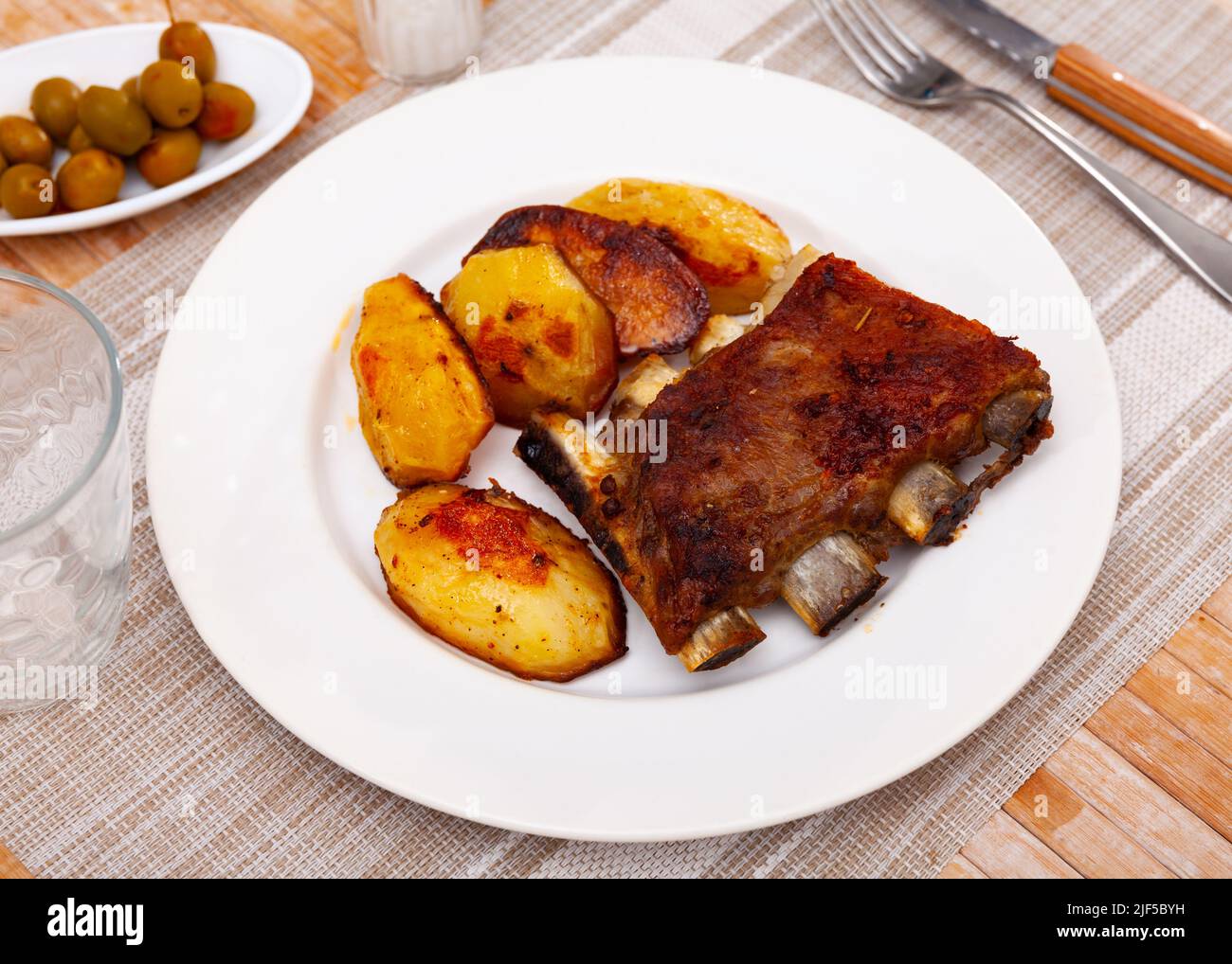 Pork ribs with boiled potatoes and spices on ceramic plate Stock Photo