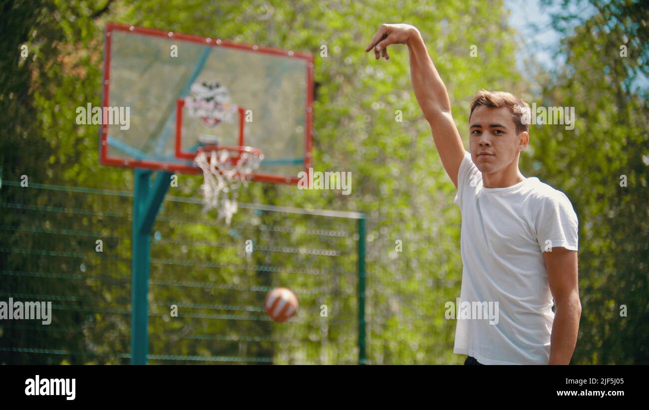 A young man throwing the ball in the basketball hoop and it gets in the target - a man looking in the camera - Mid shot Stock Photo