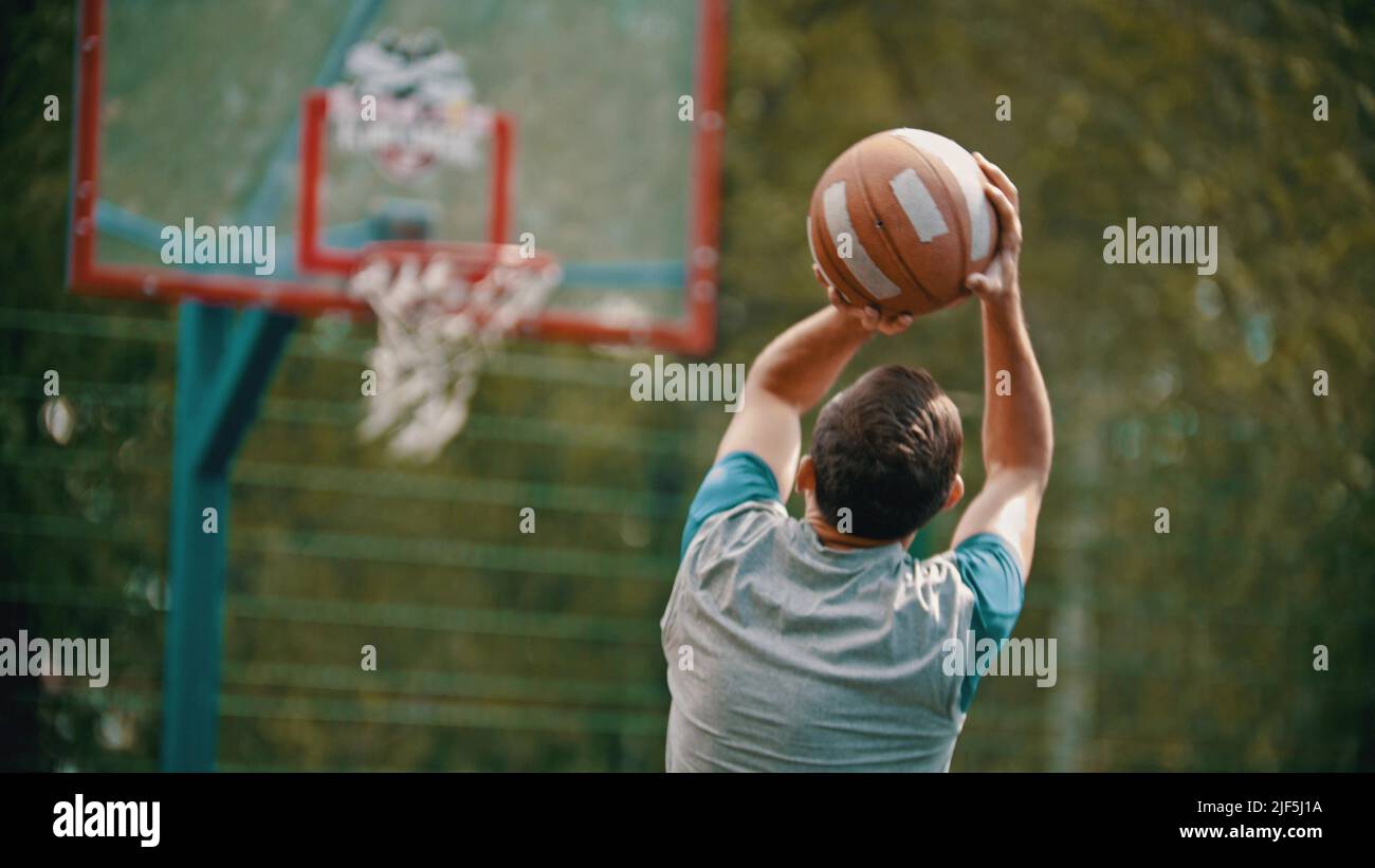 An athletic man jump and about to throw the ball in the basketball hoop - Back view Stock Photo