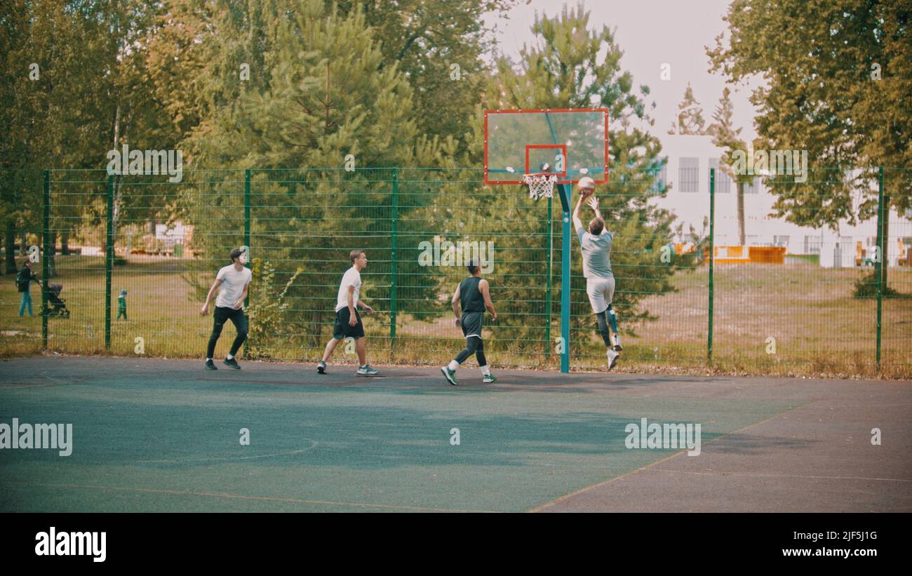 Four young friends playing basketball on the sports ground - Wide shot Stock Photo