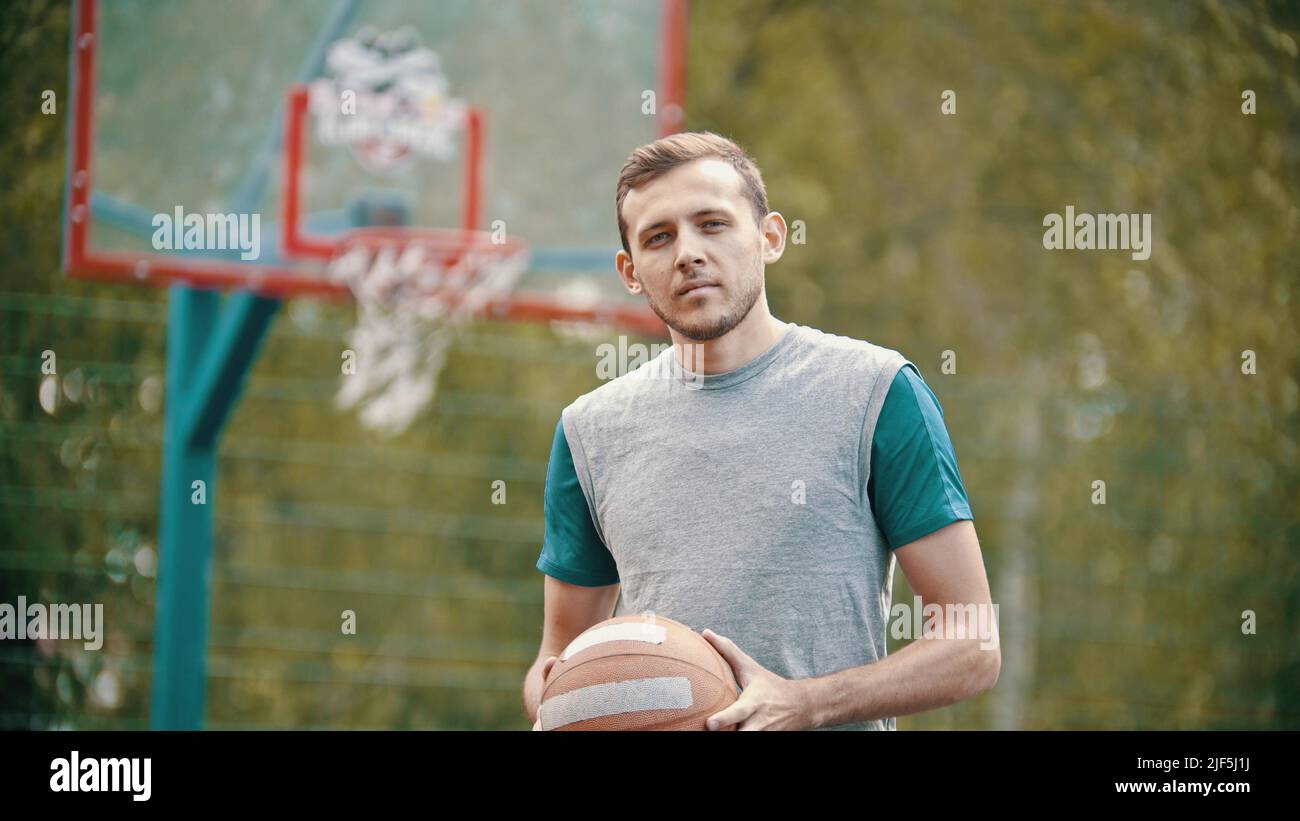 A handsome man trainer i standing on a sports ground and holding a basketball ball - Portrait Stock Photo