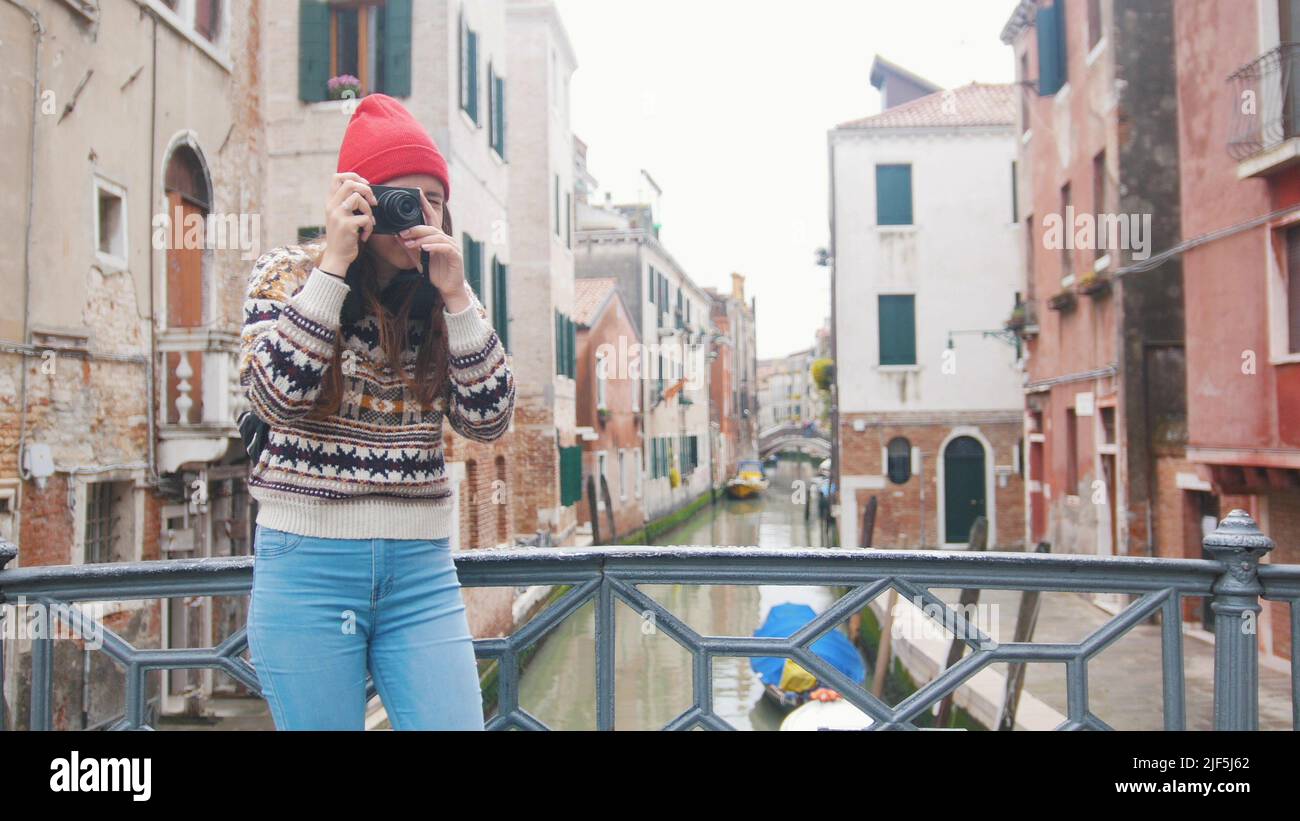 A young woman standing on the bridge and taking a photo on her camera - Venice, Italy. Mid shot Stock Photo