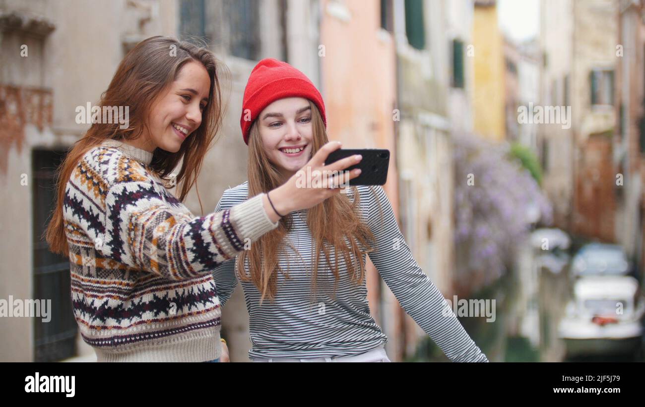 Two young women in warm clothes standing on the bridge and taking a selfie - Venice, Italy. Mid shot Stock Photo