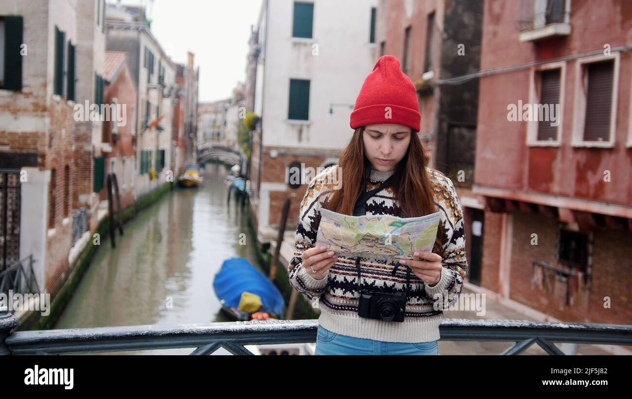 A young woman standing near the water channel and looking in her phone - Venice, Italy. Mid shot Stock Photo