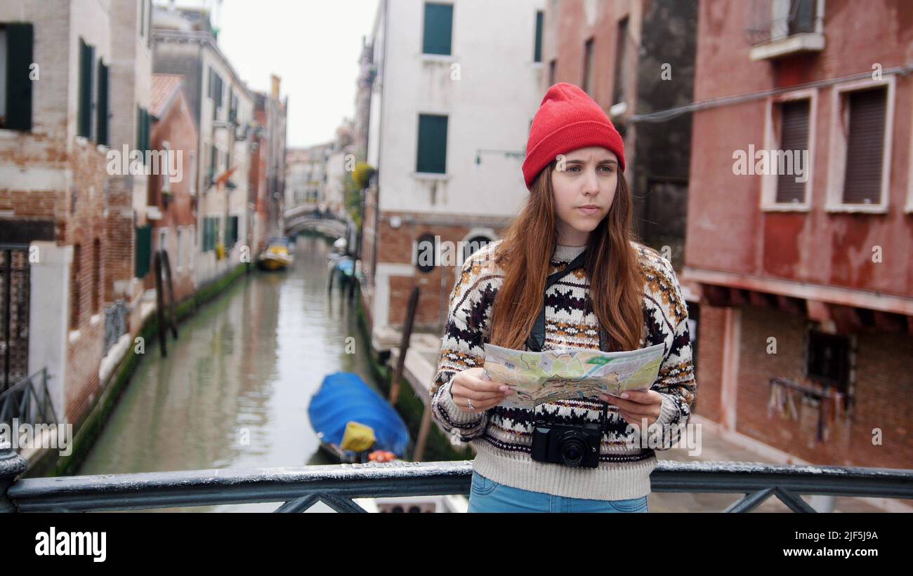 A young confused woman standing above the water channel and looking at the map - Venice, Italy. Mid shot Stock Photo
