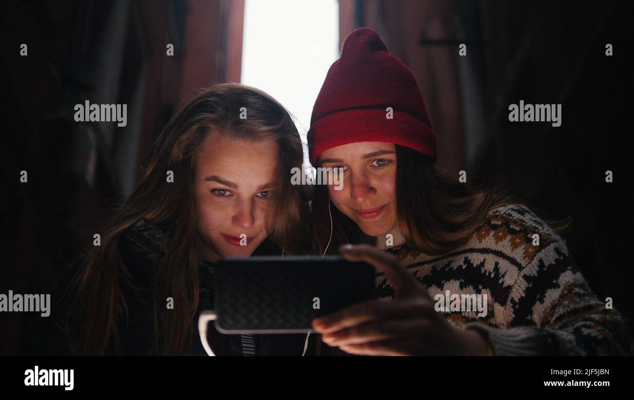 Two young smiling women looking at the phone screen with headphones. Mid shot Stock Photo