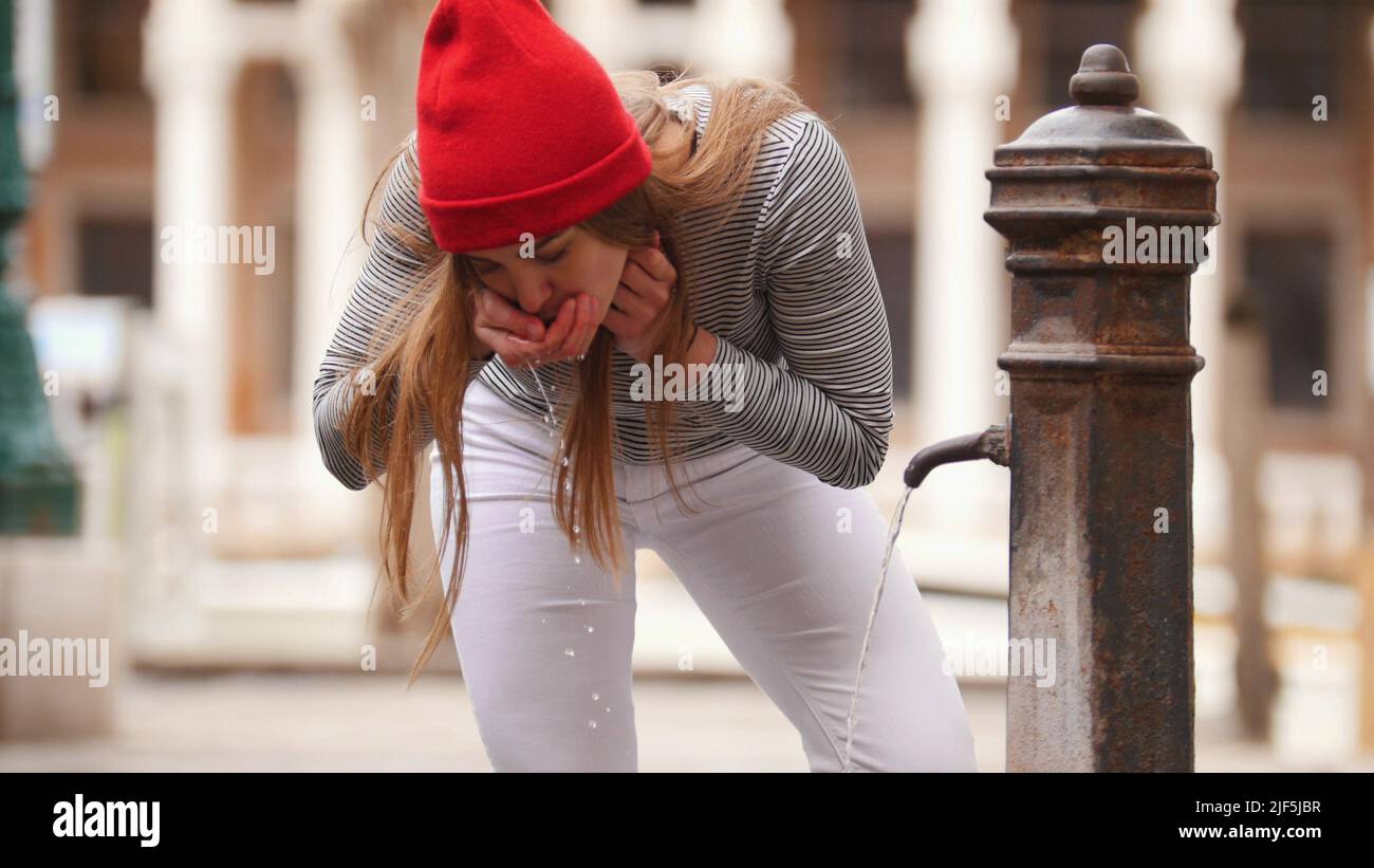 A young woman drinks water from a street fountain. Mid shot Stock Photo