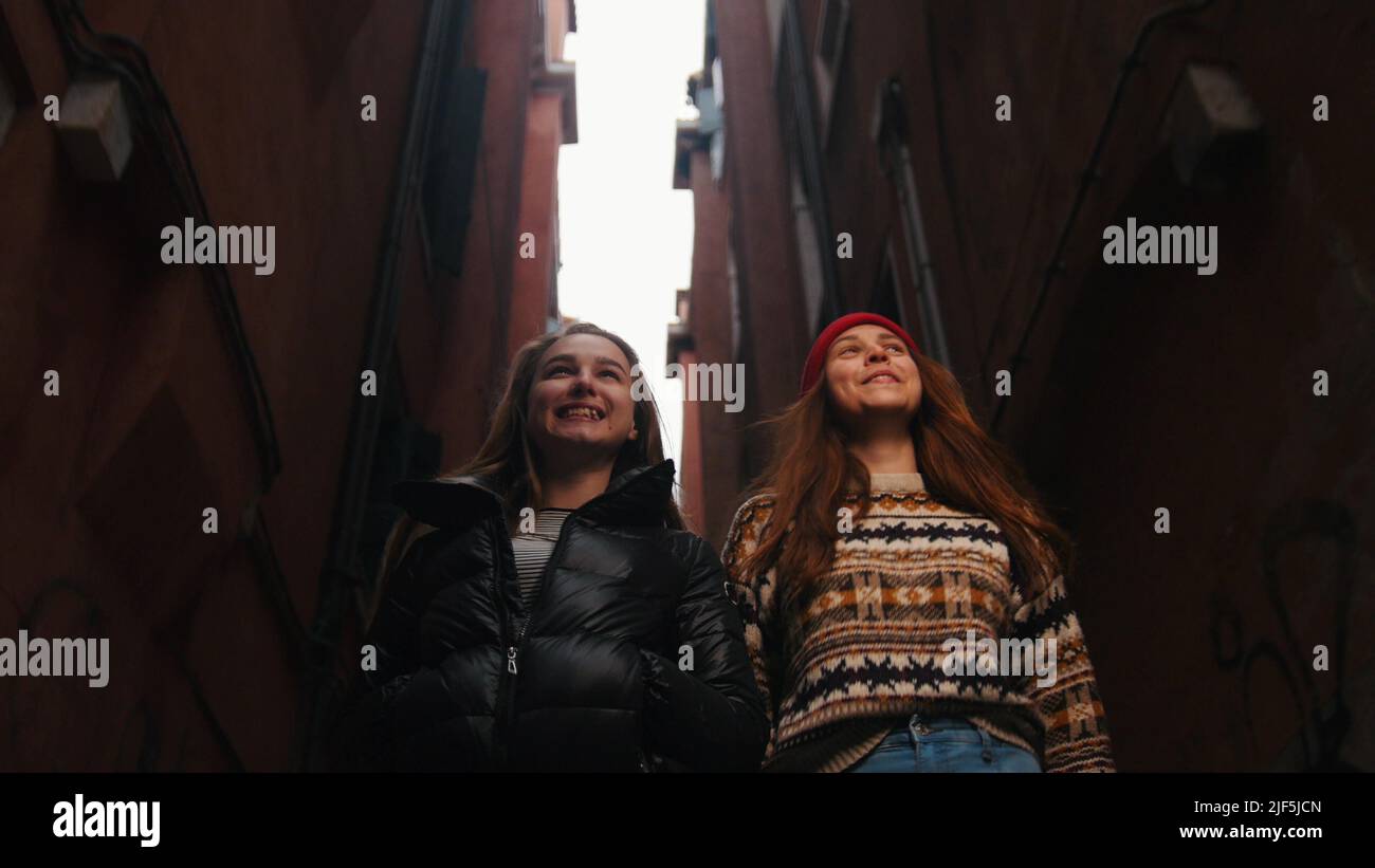 Two young smiling women walking in the narrow street. Mid shot Stock Photo