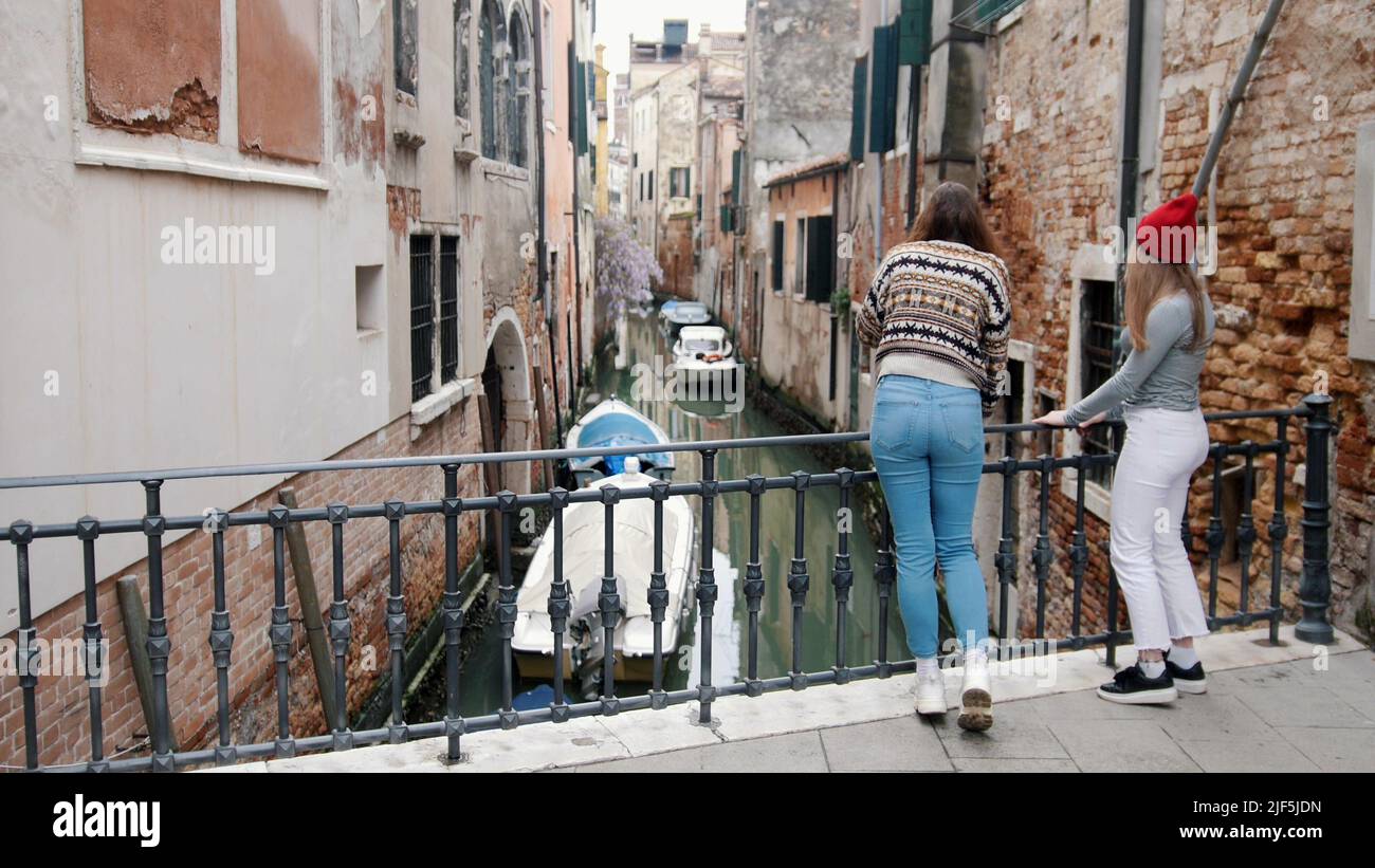 Two young women are look afar leaning on the bridge On the streets of Venice - Mid shot Stock Photo