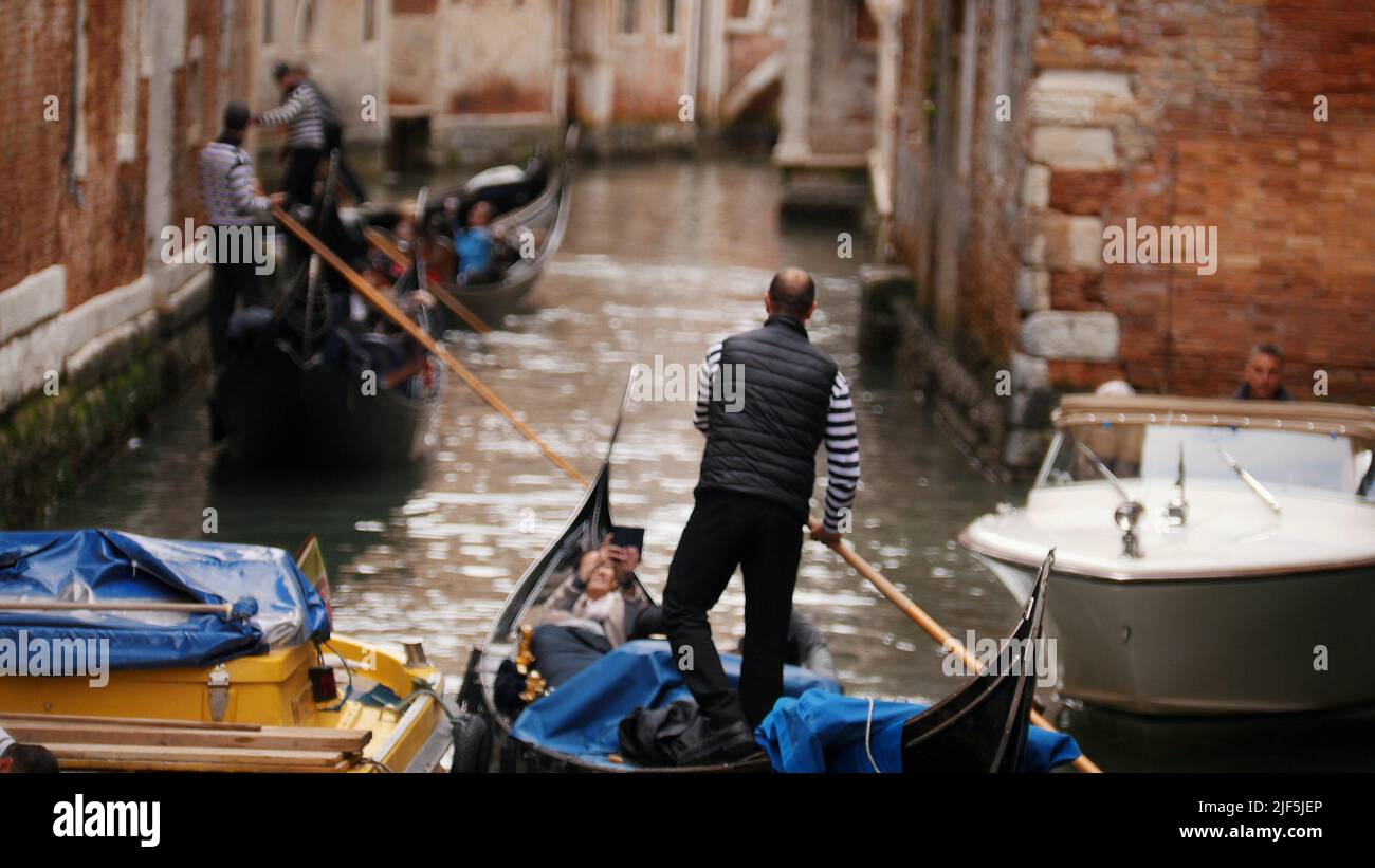 The water channel of Venice - men are rowing on a rowboat along the river - Mid shot Stock Photo
