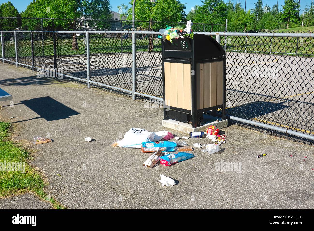 Trash bin overflowing with garbage beside a sport court in a local park. Stock Photo