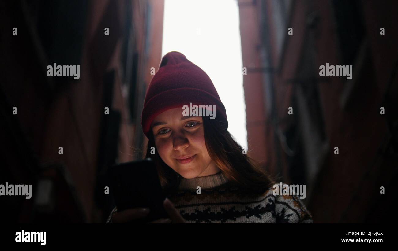 Woman on the narrow alley. Phone highlights her face - Mid shot Stock Photo