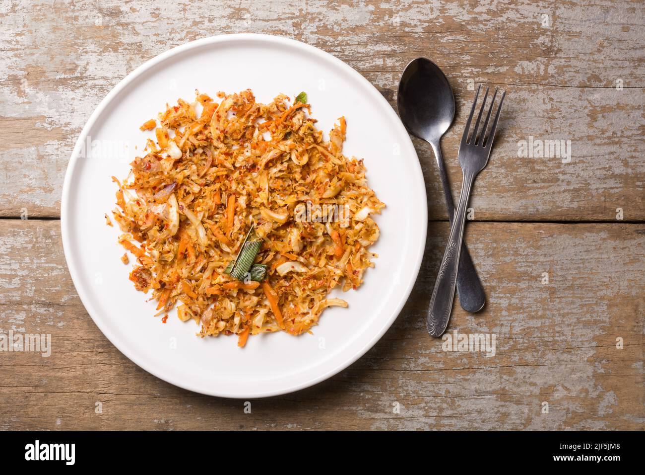 fresh healthy vegetable dish in a white plate, cabbage and carrot cooked with olive oil and herbs, sprinkled mustard seeds, placed on a table top Stock Photo